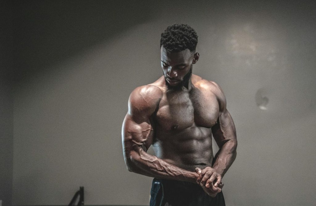 A strong, shirtless male bodybuilder showcasing muscles and strength in a gym setting.